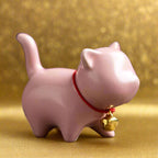Pink cat-shaped figurinewith a gold bell on a gold background