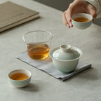 Tea ceremony setup with teacups and a teapot on a light surface.