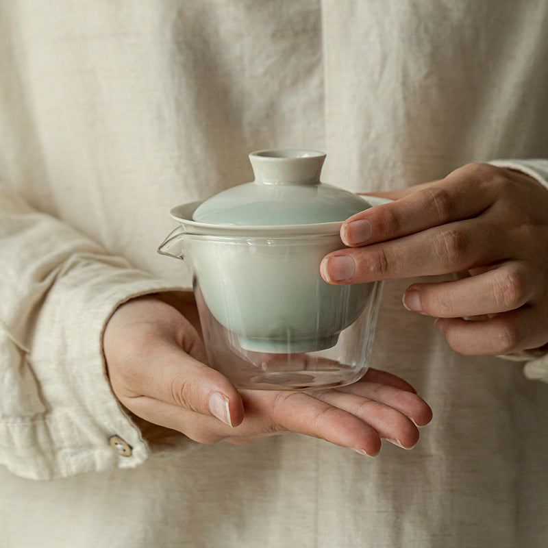 Person holding a light blue ceramic teapot with a clear glass bottom