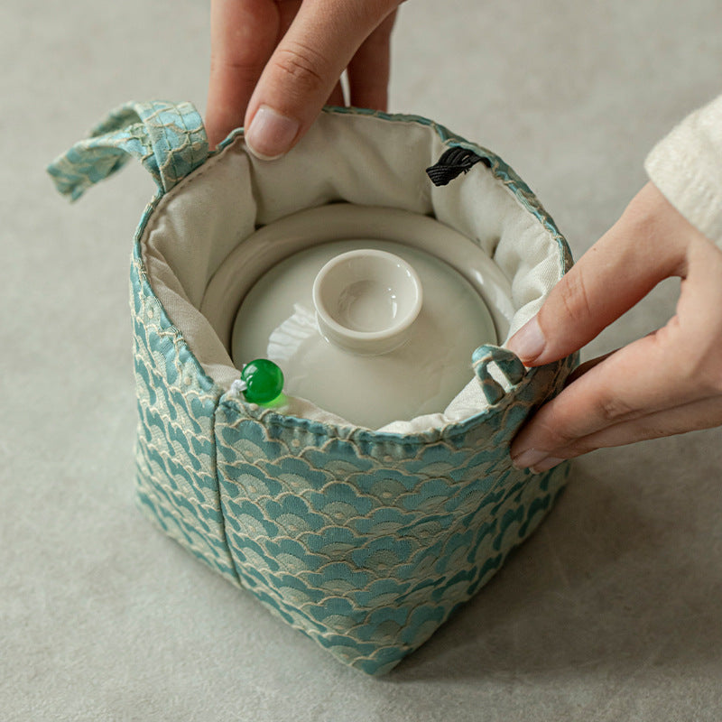 Ceramic teaset inside a green fabric pouch on a neutral background