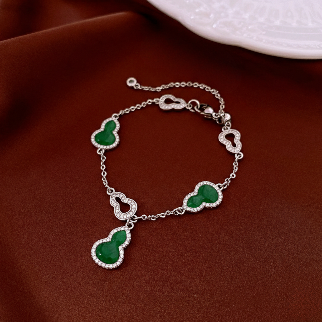Silver bracelet with green hulu-shaped charms with crystal encrusted outline on a red fabric background
