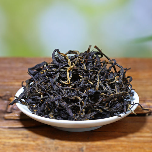 Dried black tea leaves on a white plate with a blurred natural background